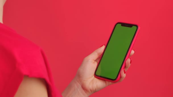女性の手は垂直位置の赤いスタジオの背景に緑のワークスペースモックアップ画面と携帯電話を保持しています。女性はインターネット上でコンテンツを閲覧します。広告エリア。テンプレートの場所。閉じろ!. — ストック動画