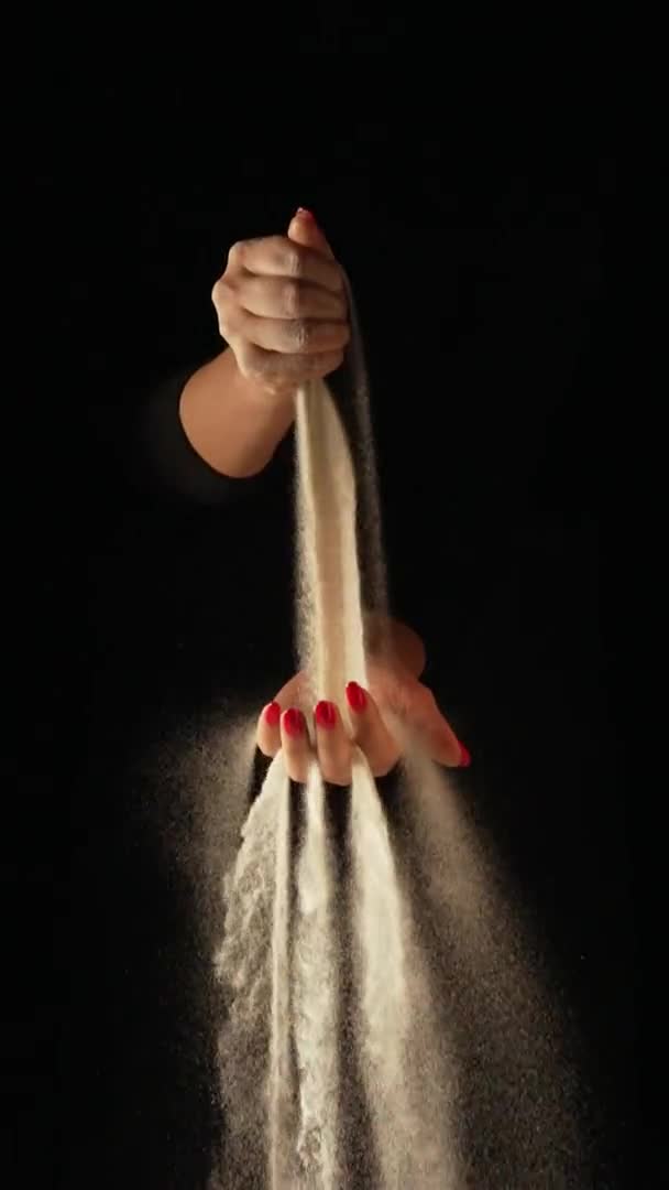 Proud suchého písku proudí do dlaně ženy a protéká jí mezi prsty na černém pozadí. Malá zrnka písku se prosévají a rozptylují ve zpomaleném pohybu různými směry. Zavřít. — Stock video