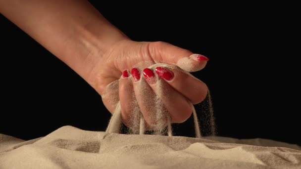 Mujer con un puñado de arena blanca y seca en sus manos, derramando arena a través de sus dedos sobre fondo negro del estudio. Primer plano de granos de cuarzo mineral natural puro en mano femenina. Movimiento lento. — Vídeos de Stock