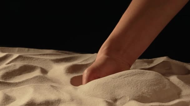 Femme avec une poignée de sable blanc et sec dans ses mains, renversant du sable à travers ses doigts sur fond de studio noir. Gros plan de grains de quartz minéral naturel pur à la main féminine. Mouvement lent. — Video