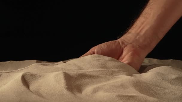 Man med handfull vit torr sand i händerna, spiller sand genom fingrarna på svart studio bakgrund. Närbild av korn av ren naturlig mineral kvarts i manlig hand. Långsamma rörelser. — Stockvideo