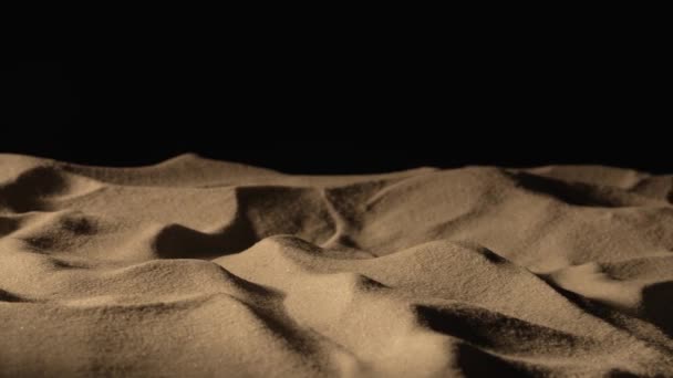 Kameran steker över högen av torr sand i mörker på svart bakgrund. Närbild av sanddyn med gryniga partiklar gnistrande i ljuset. Slow motion klar, 4K vid 59,97 fps. — Stockvideo