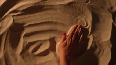 Dişi el kumlu yüzeyi düzleştiriyor ve Güneş 'i çiziyor. Kadın eli kumda resim çiziyor. Deniz kenarında yaz tatili, plajın tadını çıkarmak. Turizm sezonu. Yavaş çekim.