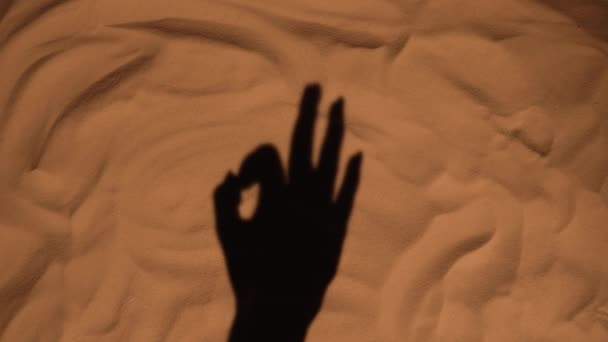 Der Schatten einer Frauenhand auf dem Sand des Strandes, der ein Zeichen von O.K. zeigt. Nahaufnahme Silhouette einer weiblichen Hand. Sommerurlaub am Meer, Urlaub am Strand. Tourismussaison. Zeitlupe. — Stockvideo