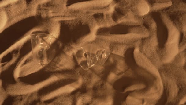 Medical mask, plastic cup and bottle falling on the sand. Coronavirus COVID-19 is contributing to pollution, as discarded masks clutter polluting beach along with plastic trash. Close up, slow motion. — Stock Video