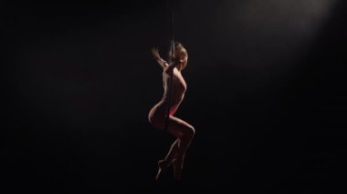 Hava halkasındaki hava akrobatları. Genç bir kadın hava çemberinde akrobatik elementler sergiliyor. Siyah arka plandaki arka plandaki karanlık stüdyoda akrobatlar var. Yavaş çekim.