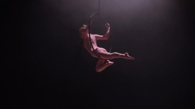 Hava halkasındaki hava akrobatları. Genç bir kadın hava çemberinde akrobatik elementler sergiliyor. Siyah arka plandaki arka plandaki karanlık stüdyoda akrobatlar var. Yavaş çekim.