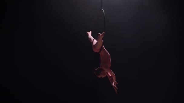 Luftakrobat i luftringen. Ung kvinde udfører de akrobatiske elementer i luftledningen. Aerialist ind på sort baggrund mørkt studie med baggrundslys. Langsom bevægelse. – Stock-video