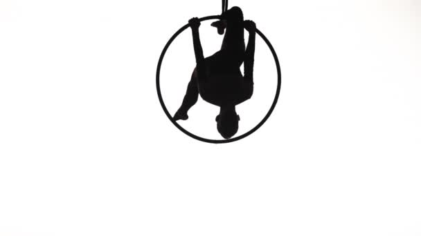 La silueta negra de una gimnasta aérea realizando trucos acrobáticos y girando en el aire en el anillo. Una joven acróbata actúa sobre un fondo de estudio blanco. Movimiento lento. — Vídeos de Stock