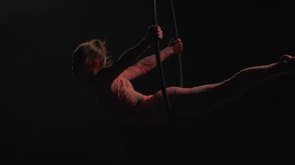 Silhouette di acrobata aerea nell'anello aereo. Giovane donna esegue gli elementi acrobatici nel cerchio dell'aria. Aerialist in su sfondo nero scuro studio con retroilluminazione. Rallentatore. — Video Stock