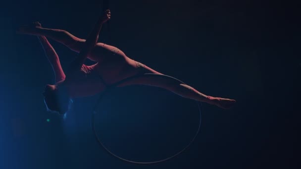 Młoda gimnastyczka wykonuje akrobatyczne akrobacje na kole powietrznym pod kopułą cyrku i demonstruje rozciąganie. Ekscytujący akrobatyczny show w ciemnym, zadymionym studio z niebieskim podświetleniem. Zwolniony ruch. — Wideo stockowe