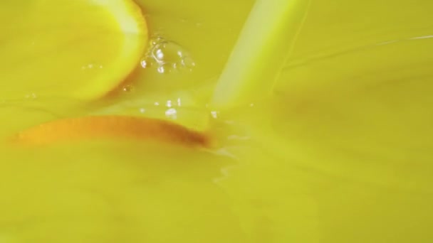Желтый апельсиновый сок с половинками апельсина. Крупный план из цитрусового экзотического сладкого нектара с оранжевыми ломтиками, закрученными в жидкости. На заднем плане свежевыжатый напиток на завтрак. Медленное движение. — стоковое видео