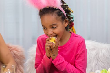 Paskalya tavuğu yiyen bir kız. Afro-Amerikalı kadın ve küçük kız evdeki dekore edilmiş odada masada oturuyorlar. Mutlu Paskalyalar. Kapat..