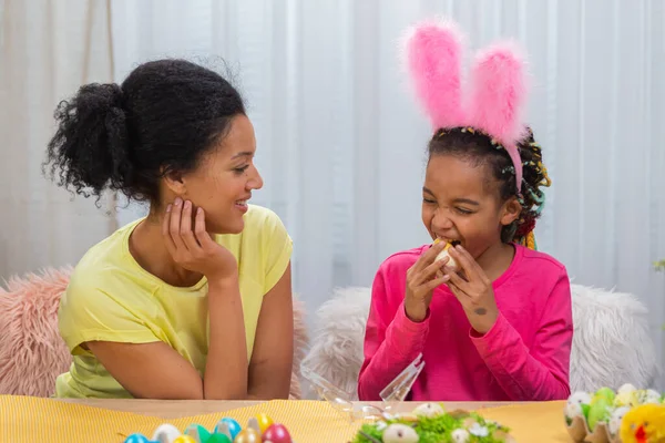 Figlia mangiare un dolce regalo di pollo pasquale. Donna afroamericana e bambina sono seduti a tavola in una stanza decorata a festa a casa. Buona Pasqua. Da vicino.. — Foto Stock