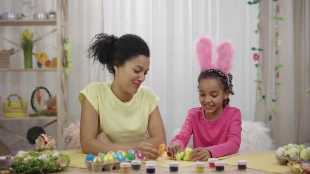 Mãe e filha com orelhas de coelho engraçado se divertir com pintos decorativos. Mulher afro-americana e menina sentada em um quarto festivamente decorado em casa. Feliz Páscoa. Movimento lento pronto 59.97fps. — Vídeo de Stock