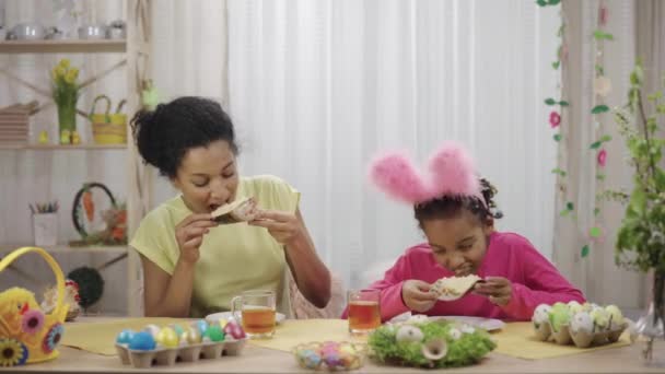 Anne ve kızı Paskalya pastasıyla çay içiyorlar. Afro-Amerikalı kadın ve küçük kız evdeki dekore edilmiş odada masada oturuyorlar. Yavaş çekim hazır 59.97fps. — Stok video