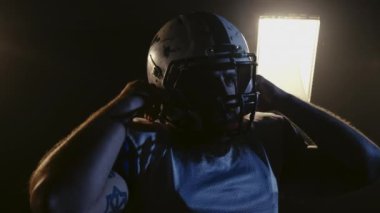 Amerikan futbol şampiyonluğu maçı: Profesyonel oyuncunun portresi, kask takmak. Üniformalı adam karanlık stadyuma giriyor. Erkeksi futbolcu. Yavaş çekim.