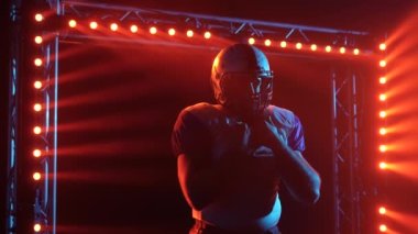 Kendine güvenen oyun kurucunun silueti uzağa bakıyor. Takım üniformalı ve kasklı Amerikalı bir futbolcu karanlıkta kırmızı ışığa karşı stadyumda duruyor. Sinema yavaş çekim. Kapat..