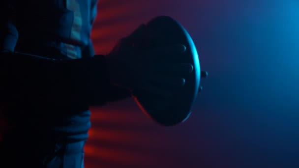 Giocatore di football americano in possesso di palla e pronto per la partita. Uomo in posa in arena buia con luci rosse e fumo. Uomo sicuro in uniforme e casco. Colpo ravvicinato. Rallentatore. — Video Stock
