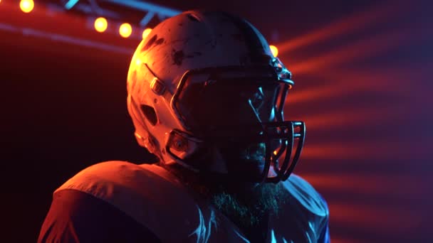 Silueta sebevědomého rozehrávače hledícího do dálky. Americký fotbalista v týmové uniformě a helmě stojí na stadionu ve tmě proti červenému podsvícení. Snímek zpomaleného filmu. Zavřít. — Stock video