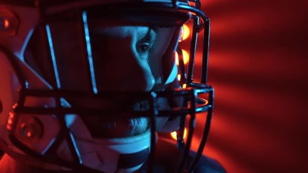 Retrato de futbolista americano profesional en casco. Hombre brutal de confianza en rojo azul retroiluminado estadio oscuro. Determinación, habilidad, concepto de poder. Estoy listo. Grabación cinematográfica en cámara lenta. De cerca.. — Vídeos de Stock