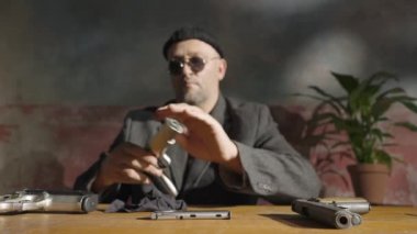 Silahı silen adamın ellerine odaklan. Leon Killer şarjörü fişeklerle çıkarır, silahı siler ve tekrar yerine koyar. Tehlikeli tetikçinin yavaş çekim filmini kapatın..