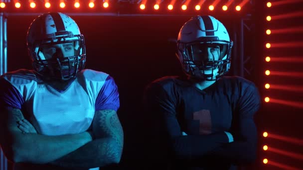 Deux quarterbacks professionnels confiants se tiennent sur le terrain sur fond de lumière rouge et de fumée. Les joueurs de football américains avant le match. Ferme là. Mouvement lent. — Video