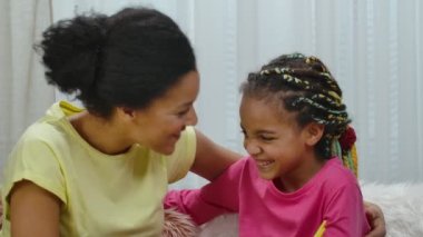 Anne ve kızı mutlu bir şekilde sarılıp gülümsüyor. Afro-Amerikalı kadın ve küçük kız evdeki dekore edilmiş odada masada oturuyorlar. Mutlu Paskalyalar. Ağır çekim. Kapat..