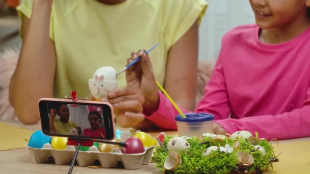 Mama i córka ze śmiesznymi króliczymi uszami kręcącymi przez telefon malujące jajka. Afroamerykanka i dziewczynka siedzą w uroczyście urządzonym pokoju. Szczęśliwego Wielkanocy. Zwolnij trochę. Zamknij się.. — Wideo stockowe