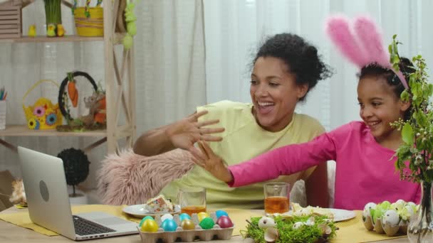 Mutter und Tochter unterhalten sich per Laptop per Videotelefonie, schlagen Eier und trinken Tee mit Osterkuchen. Afroamerikanerin und kleines Mädchen sitzen in dekoriertem Raum. Frohe Ostern. Zeitlupe. — Stockvideo