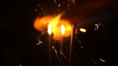 Siyah stüdyo arka planında kıvılcımlar yanıp sönüyor. Parlak Bengali havai fişekleri, karanlıkta altın kıvılcımlar saçan. Tatil kavramı, yeni yıl, parti, doğum günü. Kapatın. Yavaş çekim.