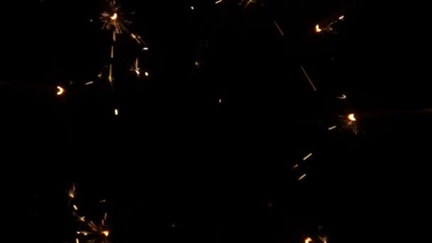 Sprankelende spetters van bengaalse vuren op zwarte achtergrond. Een bliksemschicht in het donker. Sprankelend bengali vuurwerk met gouden spatten vonken. Vakantie, nieuwjaar, verjaardag. Sluit maar af. Langzame beweging. — Stockvideo