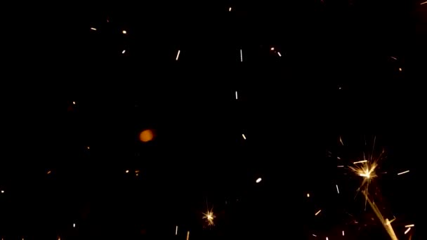 Espumantes salpicos de fogos de bengala no fundo preto. Iluminação brilhar partículas sparkler no escuro. Fogo de artifício espumante bengali com salpicos dourados de faíscas. Férias conceituais. Fecha. Movimento lento. — Vídeo de Stock
