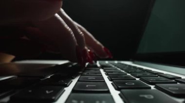 Macro Dolly, karanlık ofisteki dizüstü bilgisayarda yazı yazan kadınların sürgülü görüntülerini çekti. Kadın parmakları klavye defterine dokunur. Serbest çalışma, online eğitim. Kapatın. Yavaş çekim.