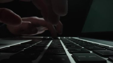 Macro Dolly, karanlık ofisteki dizüstü bilgisayarda daktilo kullanan erkeklerin sürgülü görüntülerini çekti. Erkek parmaklar klavye defterine dokunur. Serbest çalışma, online eğitim. Kapatın. Yavaş çekim.