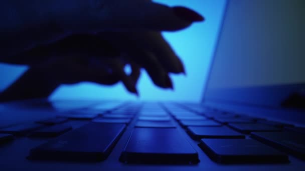 青い光で暗いオフィスでノートパソコンのキーボードを入力する女性の手の低角度ショット。ノートで働く女性。フリーランス、オンライン教育、チャット、ソーシャルネットワークでのコミュニケーション。閉じろ!. — ストック動画