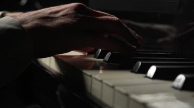Erkek piyanist karanlıkta piyanoda hızlı müzik çalar. Müzisyen parmaklarıyla telli çalgıların siyah ve beyaz tuşlarına dokunarak müzik melodisi yaratıyor. Erkek elleri yakın. Yavaş çekim 59.94fps 'te hazır..
