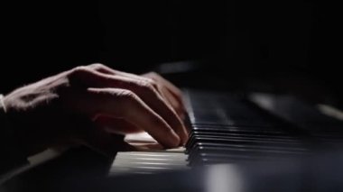 Erkek eller piyano tuşlarına dokunur ve hızlı caz melodisi çalar. Piyanist akorlar çalar karanlıkta piyanoda müzik yaratır. Müzik aletinin anahtarları. Müzisyenlerin parmakları birbirine yakın. Yavaş çekim 59.94fps 'te hazır..