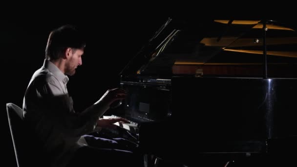 L'homme joue de la musique au piano sur fond noir. Musicien pianiste se produit dans l'obscurité tout en effectuant un concert de jazz classique sur instrument à clavier de musique. Ferme là. Mouvement lent prêt à 59.94fps. — Video