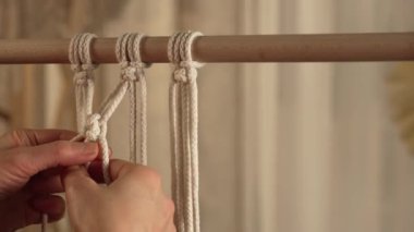Bir kadın zanaatkar atölyesindeki pamuk ipliklerden makrome örüyor. Kadın eli düğümler bağlar, dantel örer. El yapımı konsept. Yaratıcı zanaat süreci. Kapatın. Yavaş çekim.