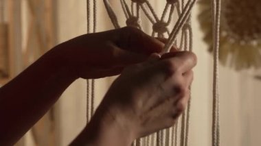 Kadın atölyesinde bir çubuğa örgü örüyor. Dişi eller düğümler bağlar ve iplikçikler oluşturur. El yapımı konsept. Dikiş işleme sürecinde olan kadınların elleri. Kapatın. Yavaş çekim.