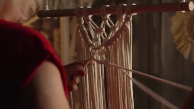 Kadın atölyesinde bir çubuğa örgü örüyor. Dişi eller düğümler bağlar ve iplikçikler oluşturur. El yapımı konsept. Dikiş işleme sürecinde olan kadınların elleri. Kapatın. Yavaş çekim.