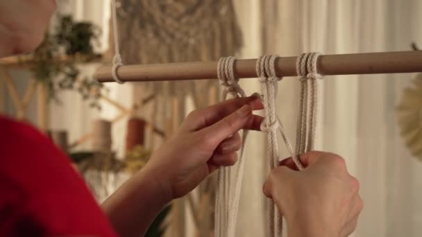 A woman craftsman weaves macrame from light cotton threads in her home workshop. Womens hands tie knots creating a lace of threads. Handmade concept. Creative craft process. Close up. Slow motion. — Stock Video