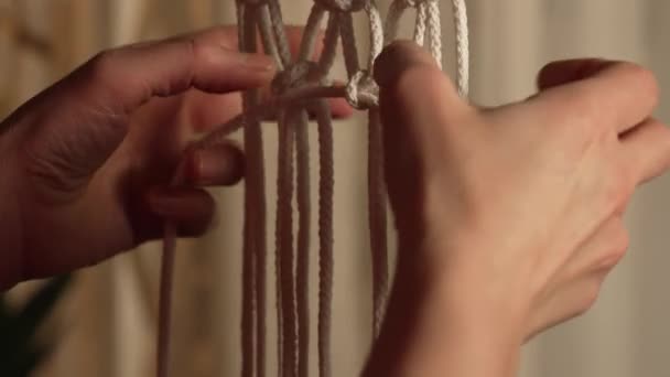 Una donna artigiana tesse macrame da fili di cotone leggeri nel suo laboratorio domestico. Le mani delle donne legano nodi creando un pizzo di fili. Concetto artigianale. Processo creativo artigianale. Chiudete. Rallentatore. — Video Stock