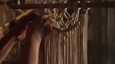 Kadınların elleri boho tarzında makrome örer. Kadın dantel yapmak için pamuk ipliklere düğüm atıyor. Yaratıcı atölye. Modern örgü doğal dekorasyon konsepti. İp ustası. Kapatın. Yavaş çekim.