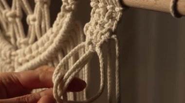 Yaratıcı bir atölyede bir kadın halat ustalığı yapıyor. Kadınların elleri makrome ipliklere düğüm atar ve yaratıcı bir dantel süsü yaratır. Boho tarzında makrome desenleri dokuyoruz. Kapatın. Yavaş çekim.