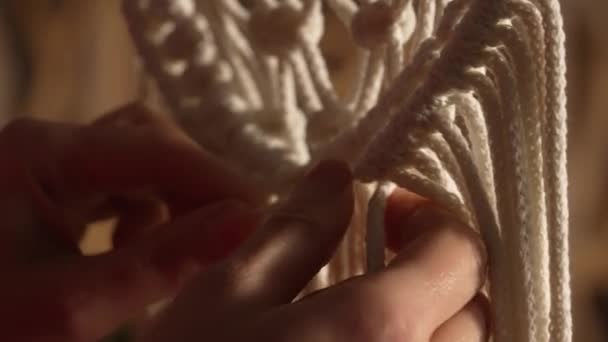 Las manos de mujer tejen macramé en estilo boho. Mujer ata nudos en hilos de algodón para crear encaje. Taller creativo. Moderno concepto de decoración natural de punto. Artesanía de cuerda. De cerca. Movimiento lento. — Vídeo de stock