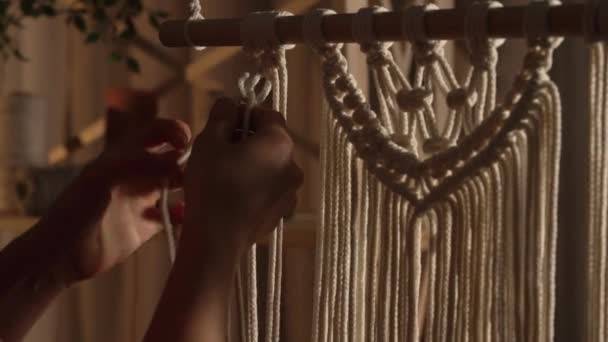 Woman weaves pattern of macrame threads with her own hands for decoration or home decor. Womans hands tying knots on ropes in a creative workshop in soft light. Handmade. Close up. Slow motion. — Stock Video