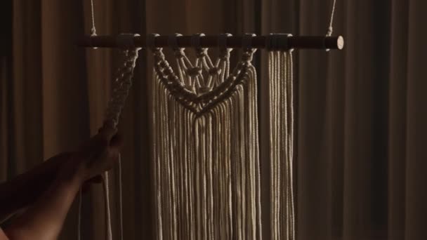 Vrouw weeft patroon van macrame draden met haar eigen handen voor decoratie of home decor. Womans handen knopen knopen aan touwen in een creatieve werkplaats in zacht licht. Handgemaakt. Sluit maar af. Langzame beweging. — Stockvideo