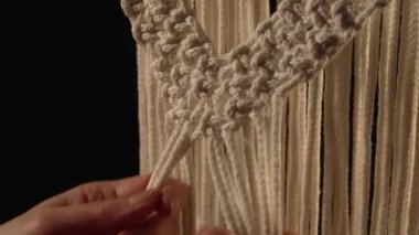 Yaratıcı atölyede kadınların elleri siyah arka planda bir makrome desen örer. Kadın dantel yapmak için pamuk ipliklere düğüm atıyor. Makromin temel düğümleri. İp ustası. Kapatın. Yavaş çekim.